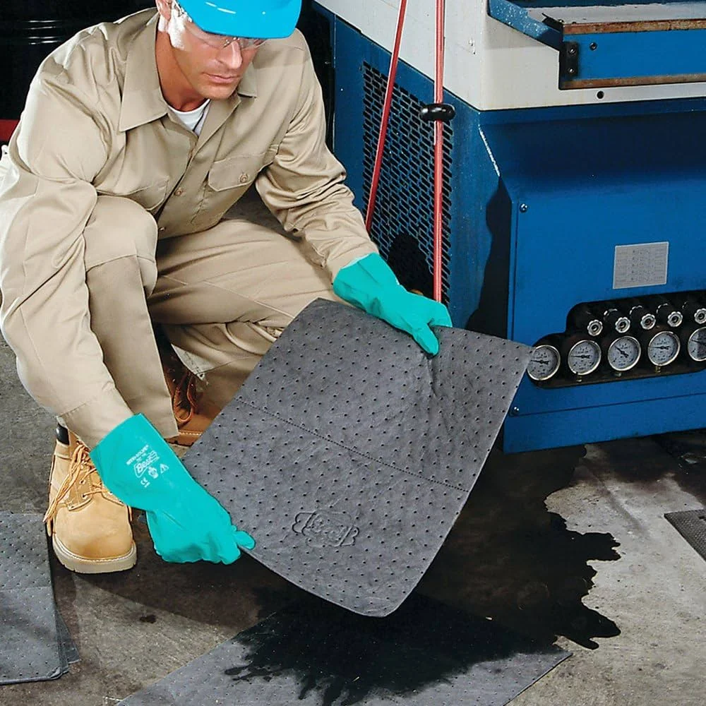 Operario aplicando una almohadilla absorbente para controlar derrames de líquidos en un entorno industrial.