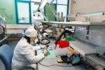 Área de trabajo ESD en industria electrónica con operaria manipulando placa PCB y sistema de protección electrostática